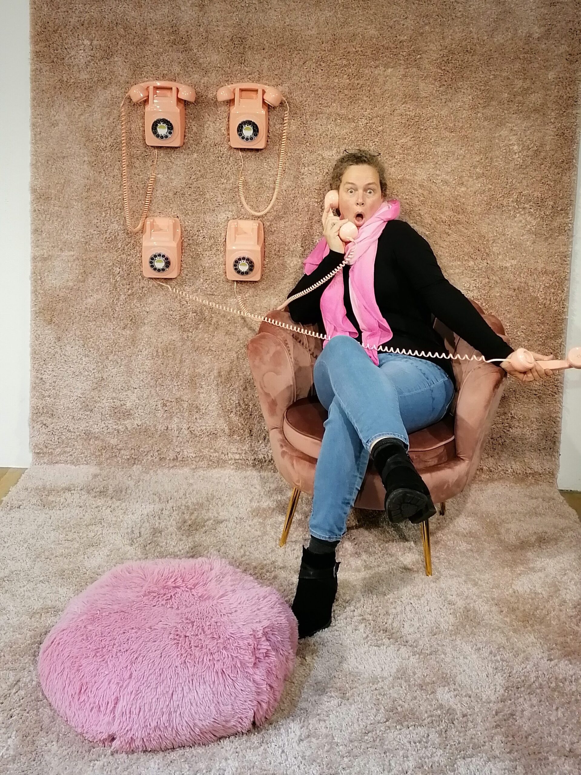 Simone sitzt mit 4 Telefonen in einem Sessel und guckt erschrocken